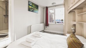 Una camera d'albergo con un letto, una doccia, una finestra vista strada e un quadro appeso al muro.