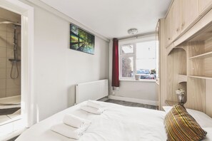 Una habitación de hotel con una cama, ducha, ventana con vistas a la calle y un cuadro en la pared.