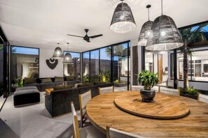 A modern interior with a round wooden dining table, dark sofas, and pendant lighting. - Villa Mujo by BaliSuperHost (Bali)