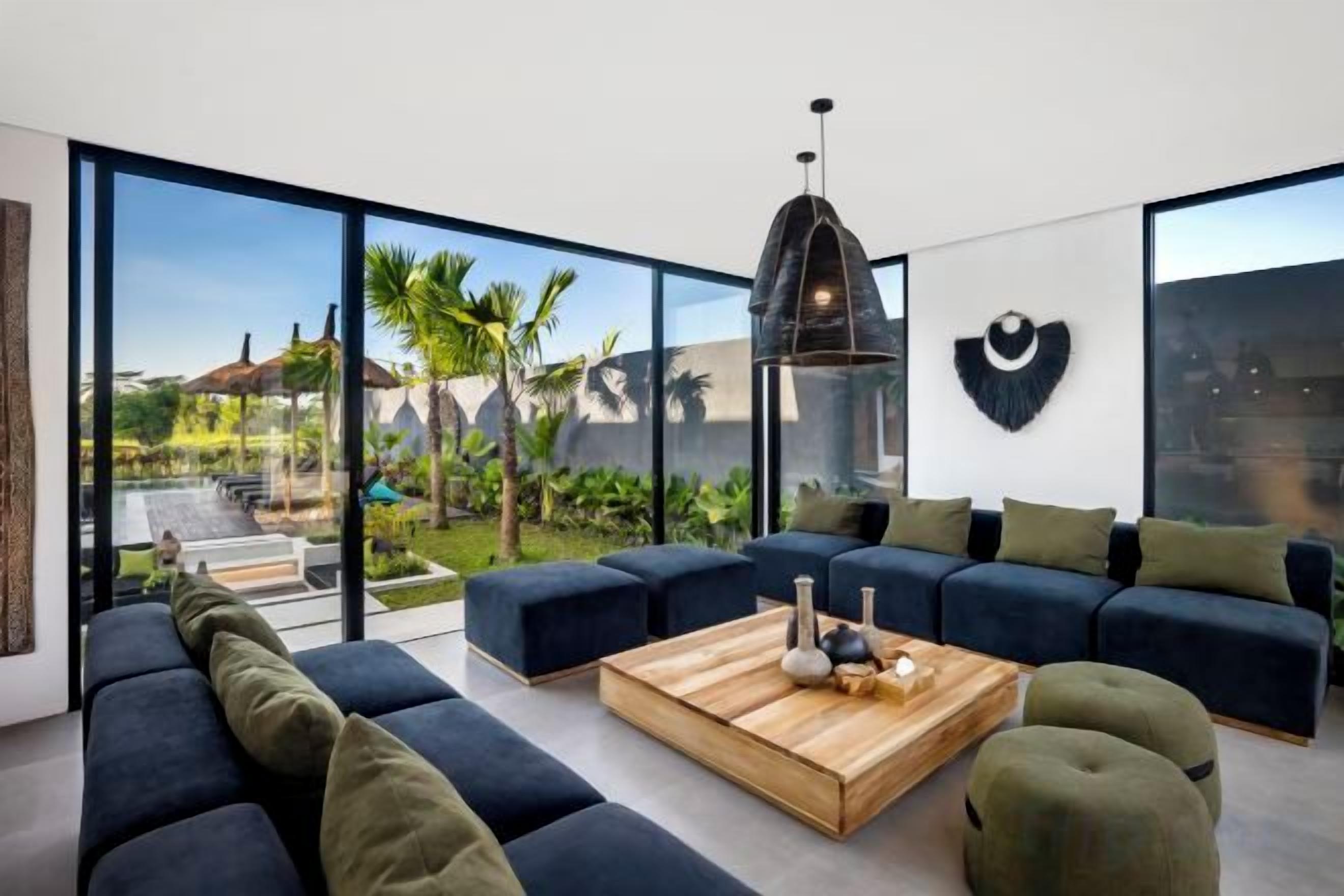Un salon moderne doté d’une grande porte vitrée donnant sur un jardin, d’un canapé bleu foncé, d’une table basse en bois et d’un luminaire suspendu.