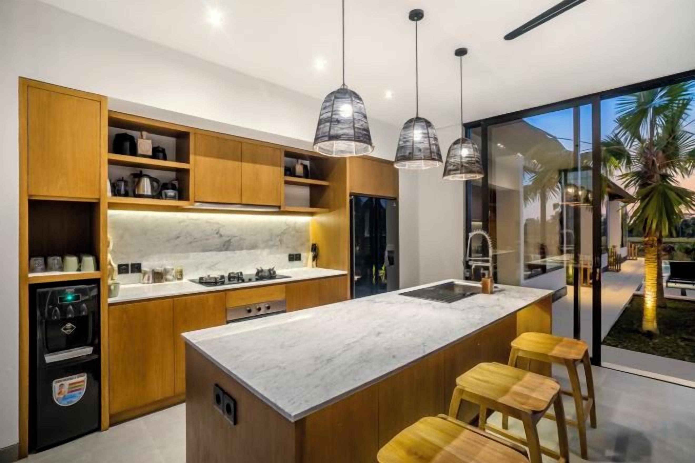 A modern kitchen with wooden cabinets, a marble countertop, and pendant lighting.
