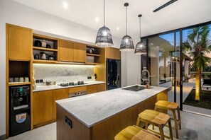 A modern kitchen with wooden cabinets, a marble countertop, and pendant lighting. - Villa Mujo by BaliSuperHost (Bali)