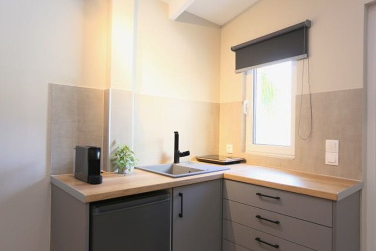 A compact kitchen with a dishwasher, a sink, and a window with a blind.
