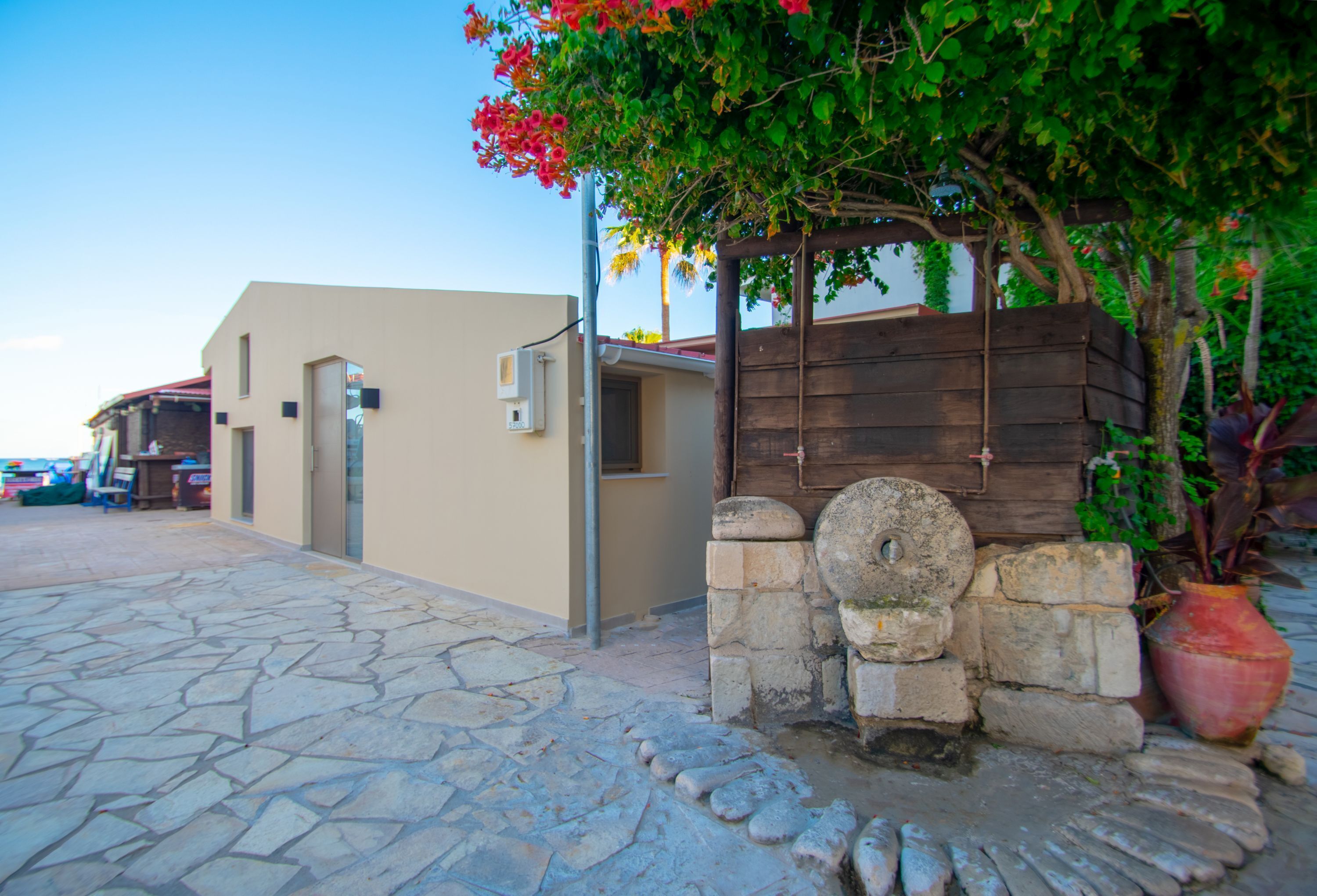 Una calle empedrada con un edificio que tiene una pérgola de madera y un muro de piedra.