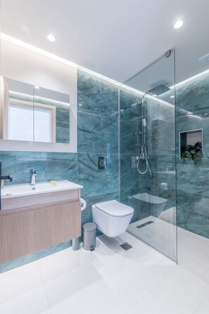 A modern bathroom with a glass shower enclosure, a white toilet, and a wooden vanity. - Manthos Beachfront Apartments (Laganas)