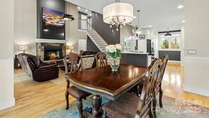 A spacious dining area with a large wooden table, comfortable seating, a fireplace, and a modern kitchen in the background.