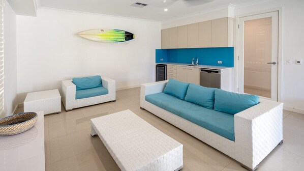 Una sala de estar moderna con un sofá grande, dos sofás más pequeños, una mesa de centro y una tabla de surf en la pared.