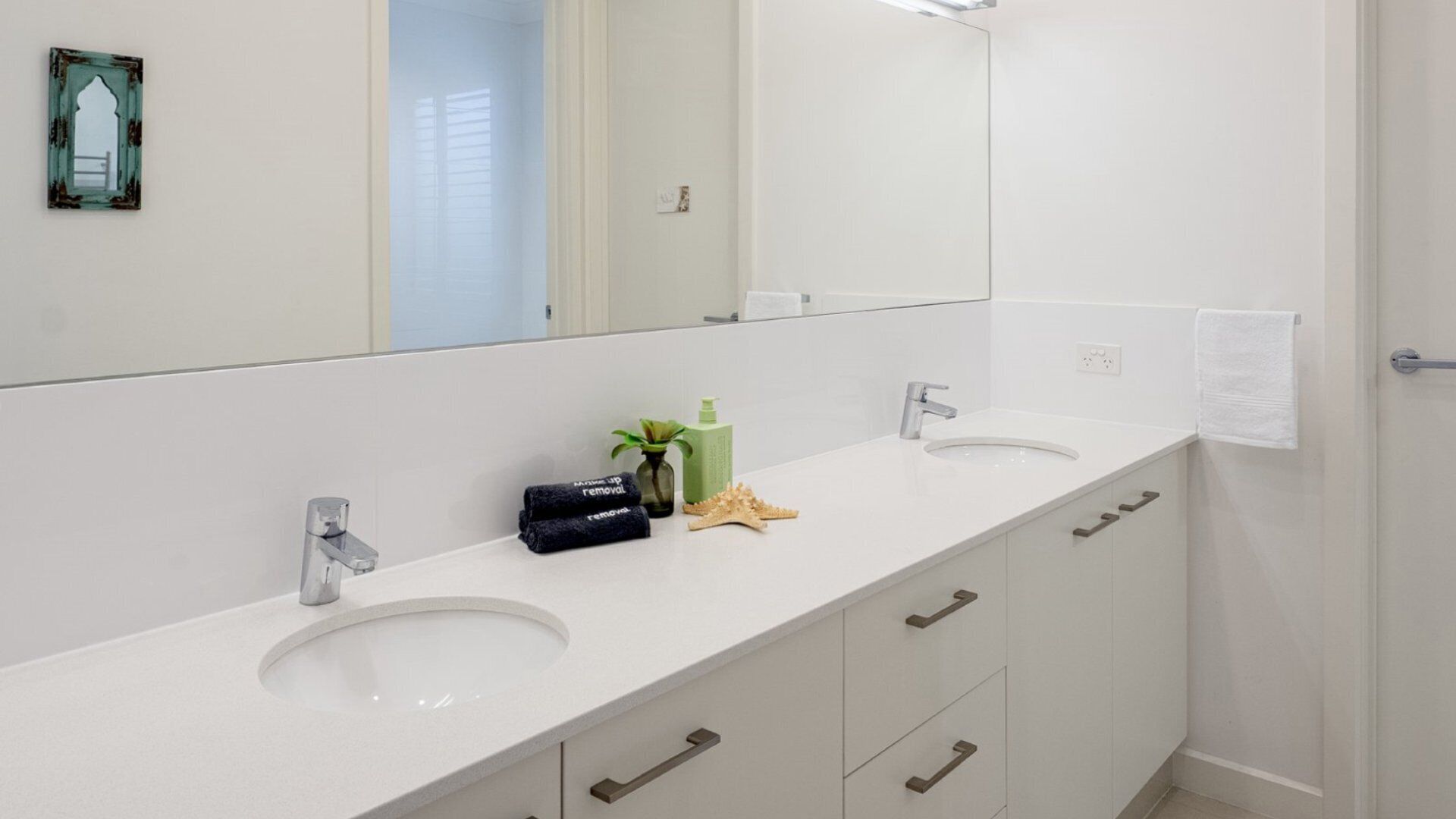 Un baño moderno con dos lavamanos, un espejo grande y un perchero para toallas.