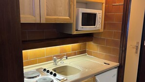 A compact kitchen with wooden cabinets, a microwave, a sink, and a dishwasher. - Studio rental at the foot of the slopes (Megève)