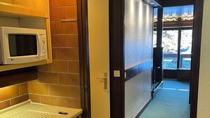 A kitchen with a microwave, a sink, and a refrigerator. There is a door leading to a hallway with a view of the outside. - Studio rental at the foot of the slopes (Megève)