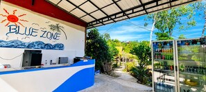 A reception area with a counter, a refrigerator stocked with beverages, and a mural with the text 'BLUE ZONE'. - Blue Zone Hostel (Koh Rong)