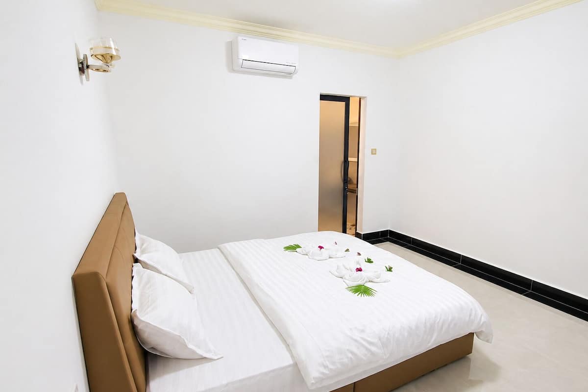 A hotel room with a bed, a wall-mounted air conditioner, and a door.