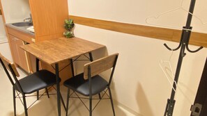 Eine kleine Küchenzeile mit Spüle und Schränken, ein Holztisch mit zwei Stühlen und ein kleiner Blumentopf.