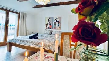 A bedroom with a bed, a table with candles, a vase with roses, and a painting on the wall.
