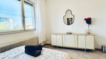 A bedroom with a bed, a radiator, a window, a dresser, and a mirror.