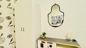 Una habitación con un armario blanco, un pequeño escritorio blanco con espejo, y un estampado de flores en el papel tapiz.