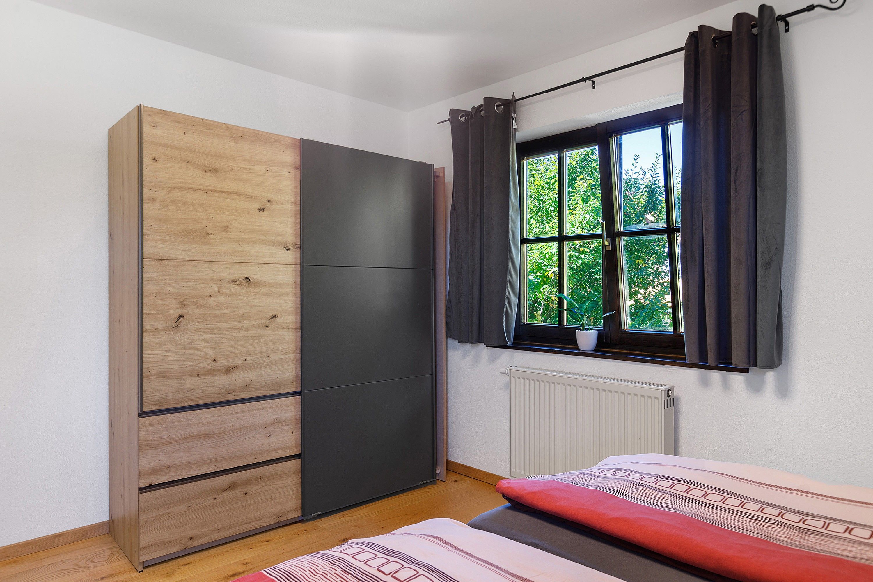 Ein Schlafzimmer mit Kleiderschrank, einem fenster mit Vorhängen, einem Heizkörper und einem Bett.