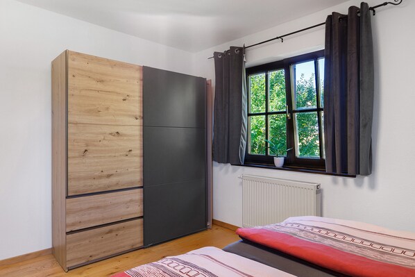 Une chambre avec un placard, une fenêtre avec des rideaux, un radiateur et un lit.
