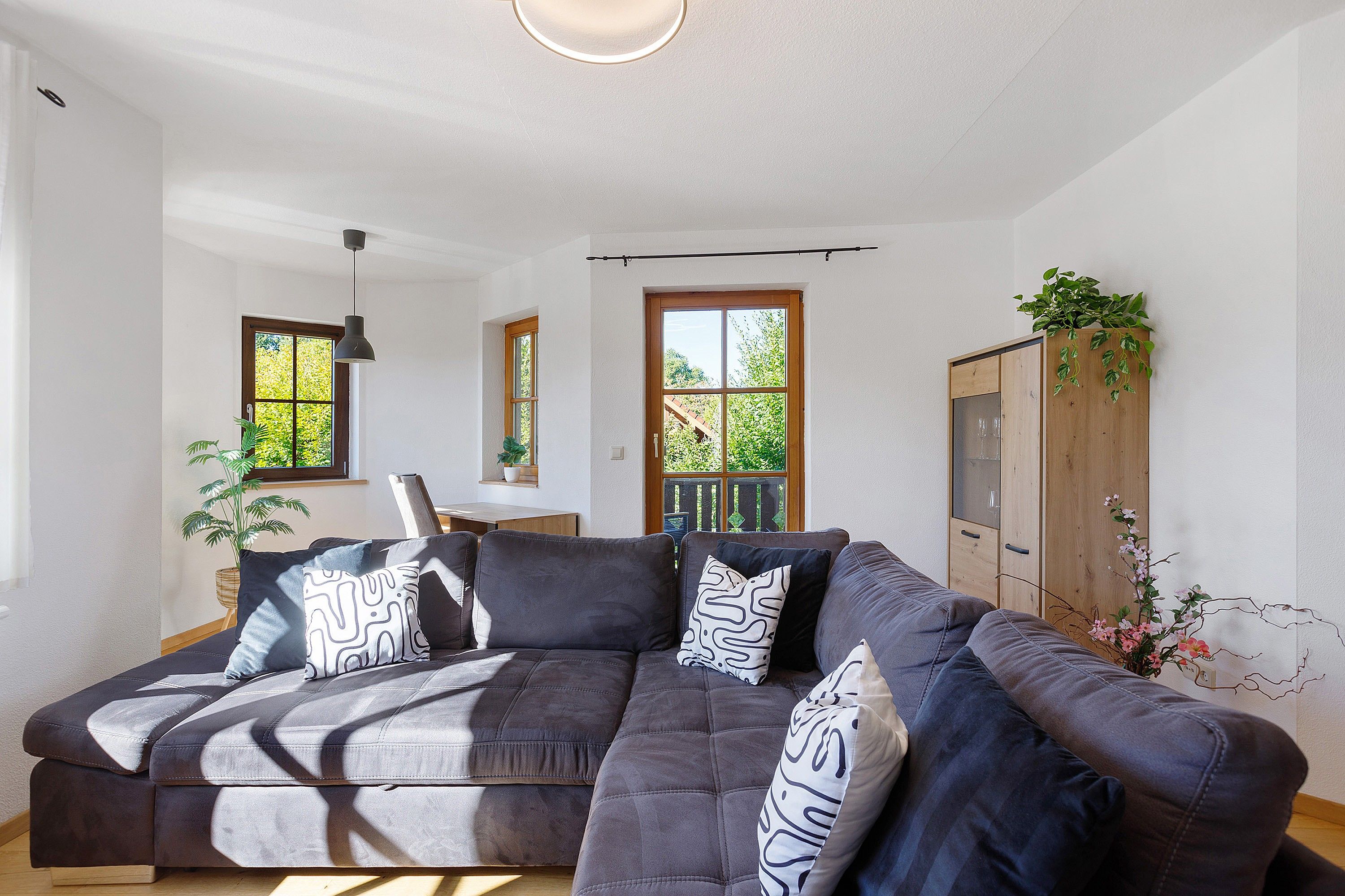 Un salon moderne avec un canapé d’angle, un meuble en bois et une plante en pot.