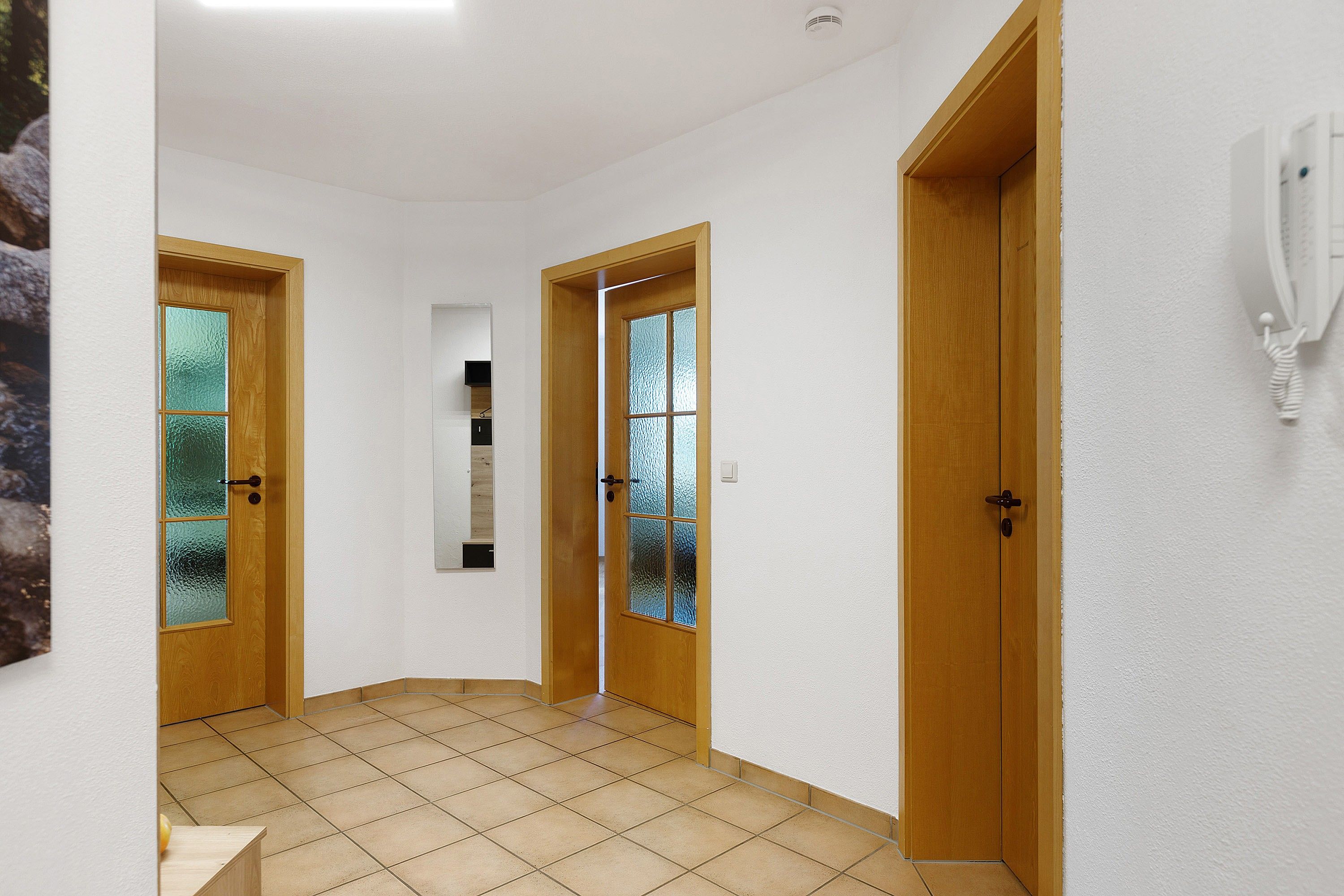 Ein Flur mit zwei Holztüren, eine davon mit einer Milchglasscheibe, und einer weißen Wand mit einem angebrachten Telefon.
