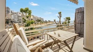 A balcony with wooden furniture, a view of the sea, and buildings in the background. - Sunny Apartment Next to the sea Amazing View (Piraeus)