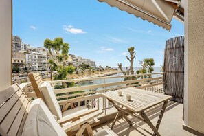 A balcony with wooden furniture, a view of the sea, and buildings in the background. - Sunny Apartment Next to the sea Amazing View (Piraeus)