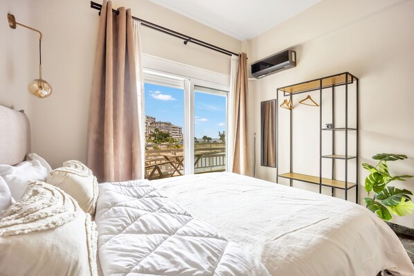 A bedroom with a large bed, a view of the beach, a wardrobe, and a plant. - Sunny Apartment Next to the sea Amazing View (Piraeus)