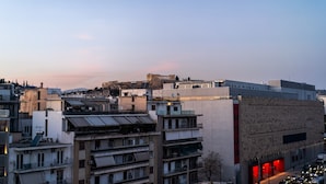 A cityscape with modern buildings, a prominent red-lit structure, and a distant hill. - Sunny 3bd Flat Acropolis View (Athens)