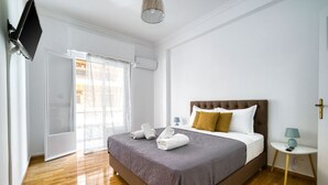 Une chambre d’hôtel avec un grand lit, un téléviseur à écran plat fixé au mur, une petite table de chevet avec une lampe et une fenêtre avec des rideaux.