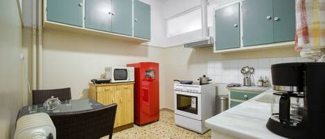 A compact kitchen with teal cabinets, a microwave, a red refrigerator, a stove, and a coffee maker.
