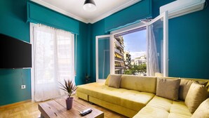 Un salon aux murs de couleur turquoise, avec un canapé jaune, une table basse en bois et une grande fenêtre donnant sur des immeubles.