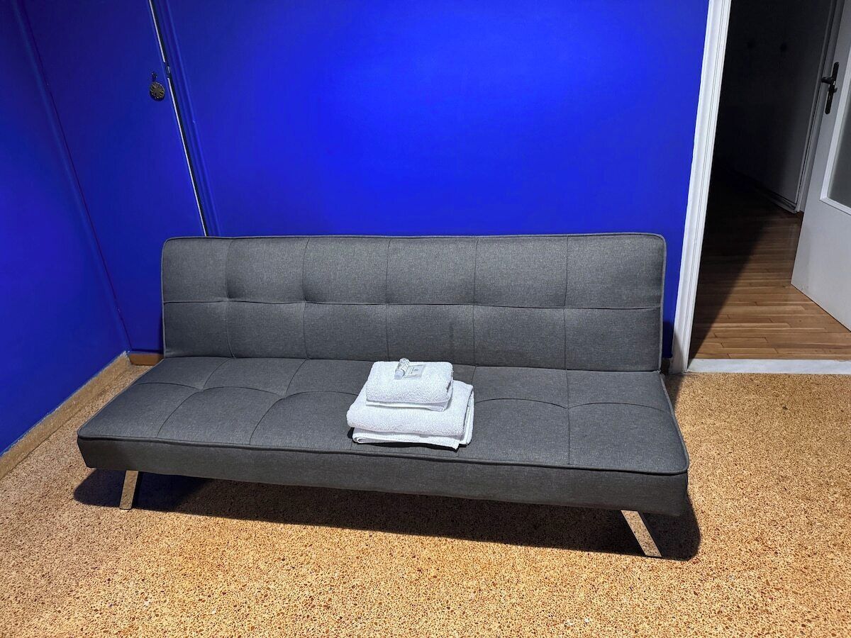 Un canapé gris sur lequel est posé un plaid blanc plié et une serviette blanche pliée, le tout placé sur un sol à motifs devant un mur bleu.