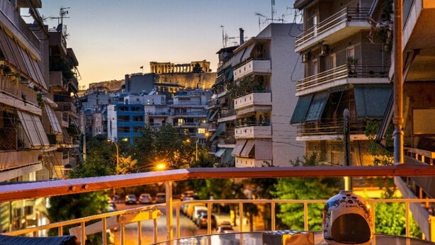 Un balcon avec une table et un vase décoratif, d’où l’on peut admirer un paysage urbain avec des bâtiments et, au loin, un monument historique.