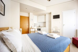 Ein Hotelzimmer mit einem Bett, einem Schreibtisch, einem Sessel, einem Fernseher und einer Küchenzeile.