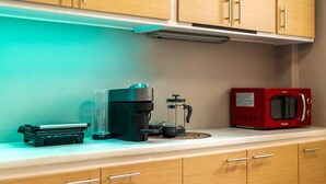 A kitchen with wooden cabinets, a coffee maker, a French press, a teapot, and a red microwave. - Sunny Cozy 3bd apt Just a min Away to Acropolis (Athens)