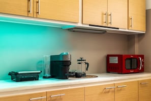 A kitchen with wooden cabinets, a coffee maker, a French press, a teapot, and a red microwave on the countertop. - Sunny Cozy 3bd apt Just a min Away to Acropolis (Athens)
