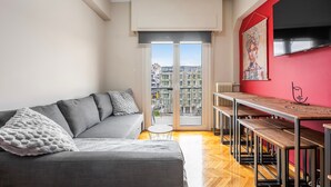 A modern living room with a grey sofa, a small round table, and a dining area with benches. - Sunny Cozy 3bd apt Just a min Away to Acropolis (Athens)