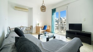 A modern living room with a sofa, a glass coffee table, a TV, and a balcony with a view of buildings. - Sunny Penthouse in Koukaki - Next to Acropolis (Athens)
