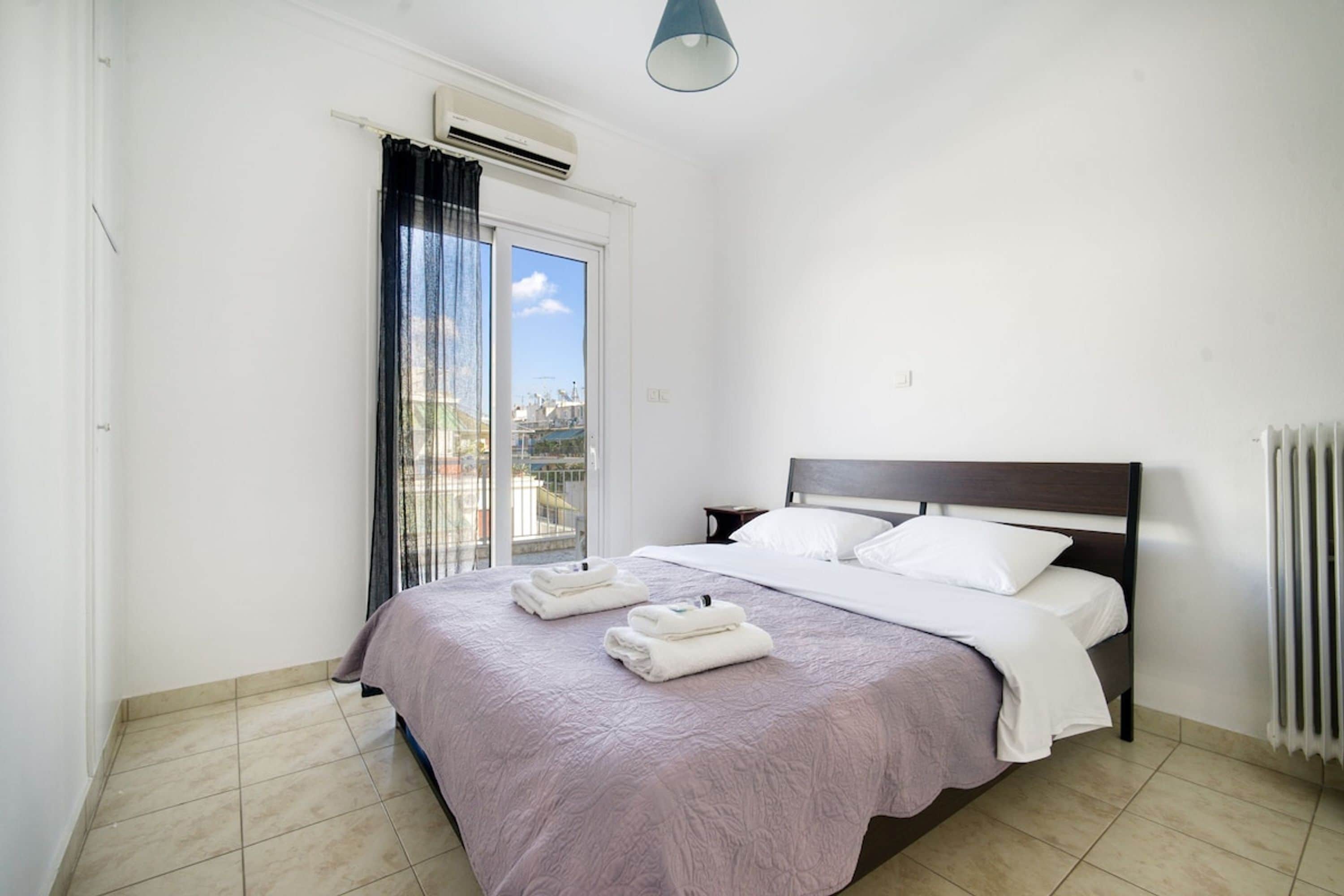 Un dormitorio con cama, ventana con cortinas, aire acondicionado y radiador.
