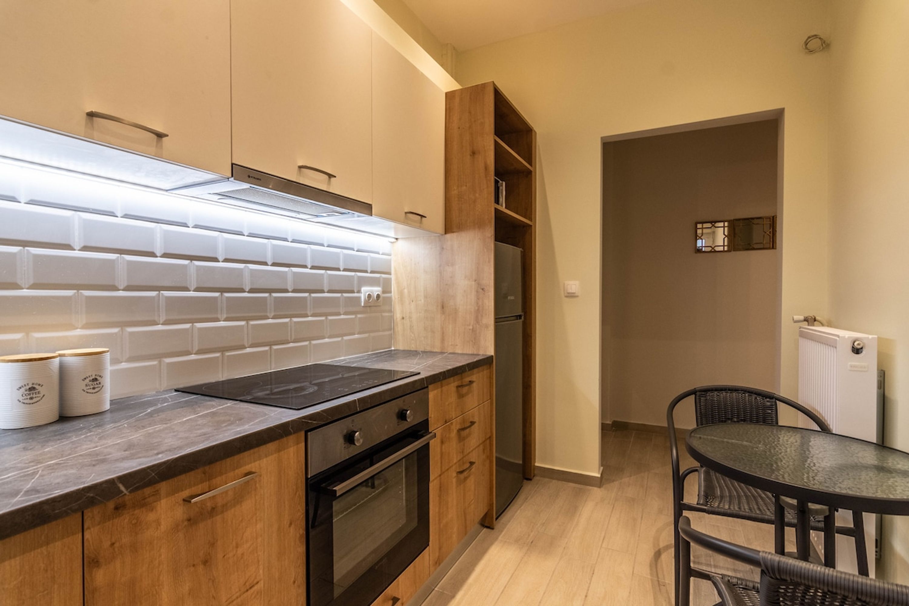 A modern kitchen with wooden cabinets, a black countertop, and a built-in oven. There is a dining area with a round table and chairs.