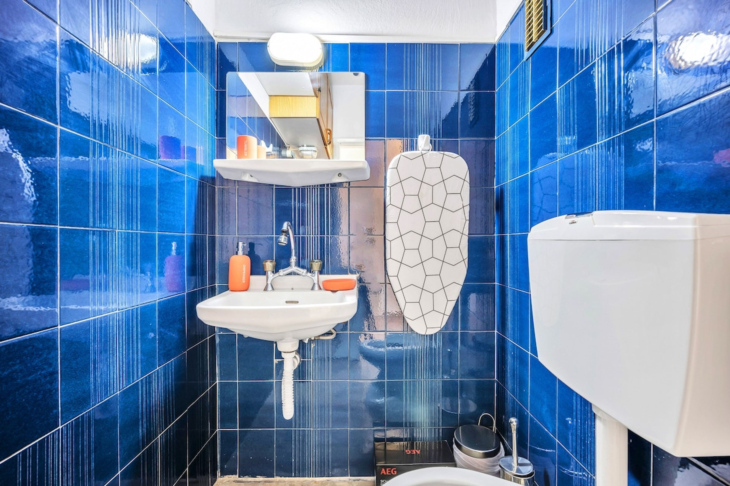 Une salle de bain avec des murs recouverts de carreaux bleus, un lavabo blanc, un miroir et des toilettes.