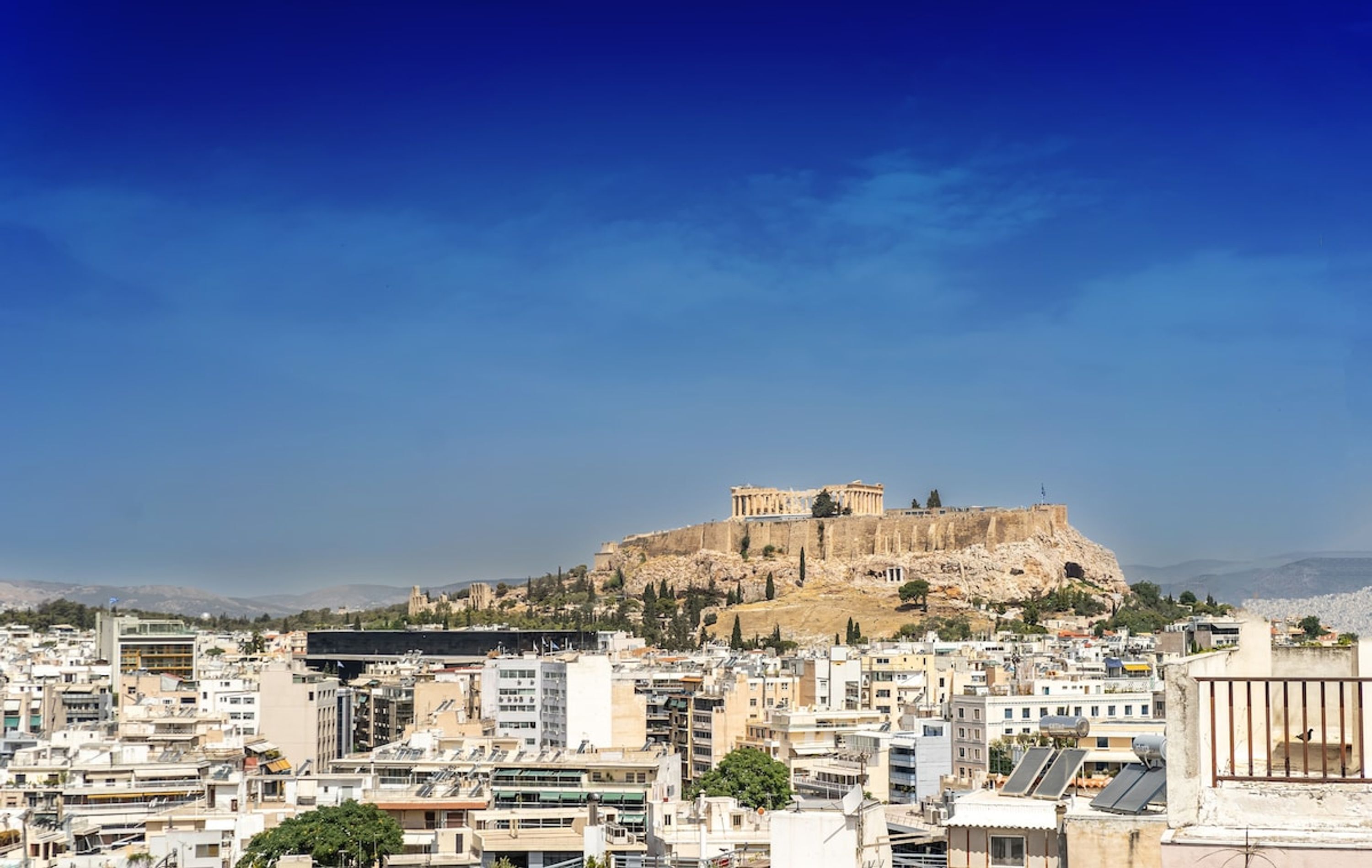 Une vue urbaine avec une imposante citadelle antique, située sur une colline et entourée de bâtiments modernes.