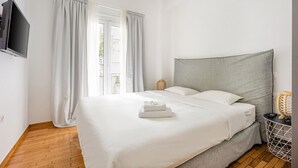 A neatly made bed with white linens, a grey headboard, and a small bedside table with a lamp. - Modern Cozy Apartment (Athens)