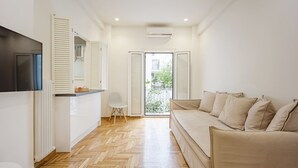 A modern apartment with a wooden herringbone floor, a beige sofa, a flat-screen TV, and a sliding glass door leading to a balcony. - Modern Cozy Apartment (Athens)