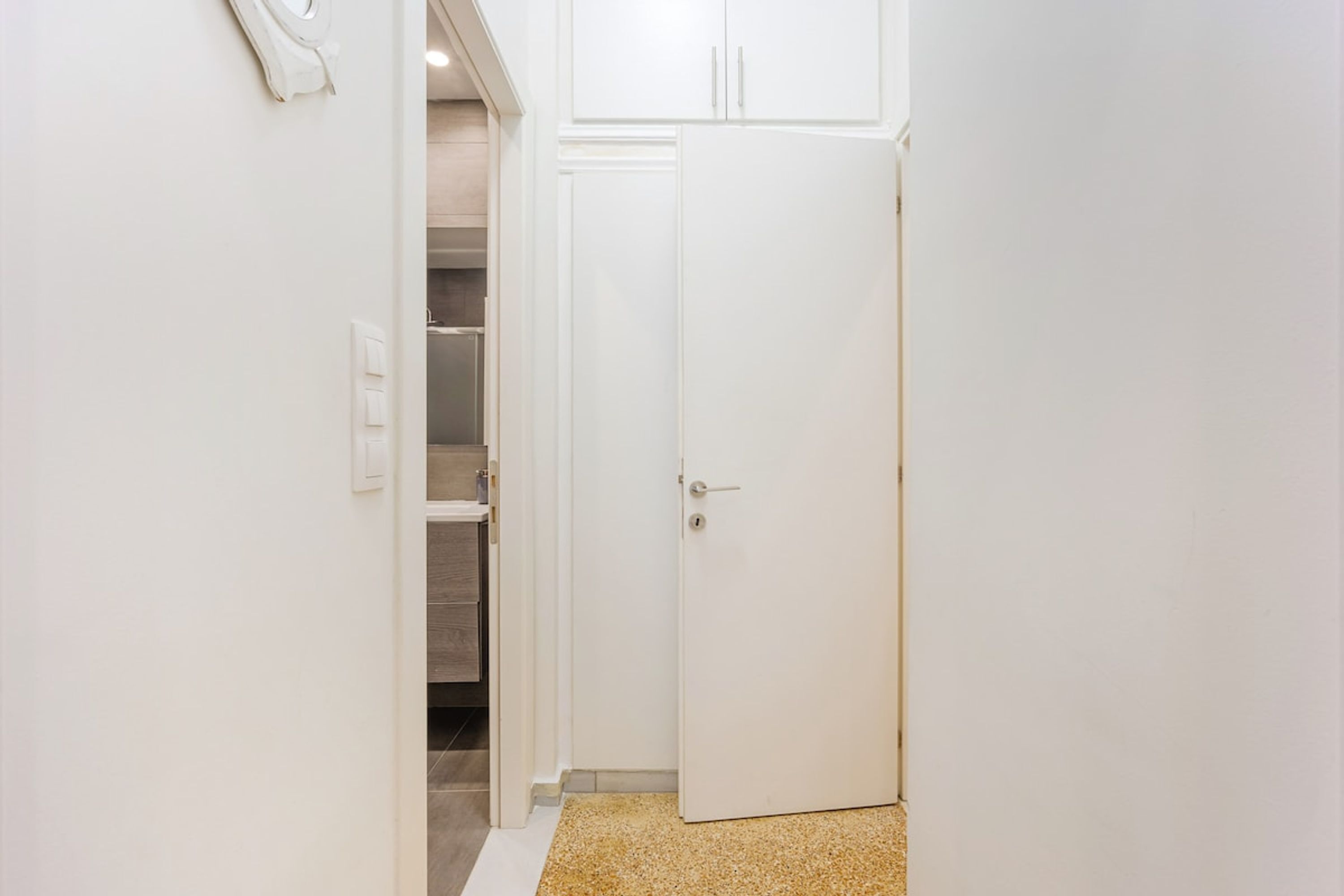 A narrow hallway with a white door at the end, a white wall, and a light switch.