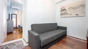 Ett modernt vardagsrum med en grå soffa, en målning som föreställer ett berglandskap och ett trägolv.