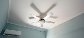 Um ventilador de teto com quatro lâminas em um quarto com paredes azul-claras e teto branco.