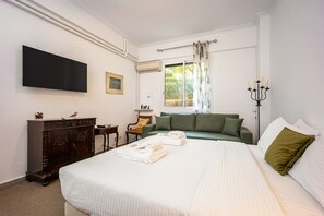 Ein Hotelzimmer mit einem großen Bett, einem flachbildfernseher an der Wand, einer Holzkommode, einem grünen Sofa und einem Fenster mit Vorhängen.