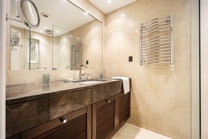Ein modernes Badezimmer mit Marmorwaschbecken, dunklem Holzschrank, großem Spiegel und Handtuchhalter.