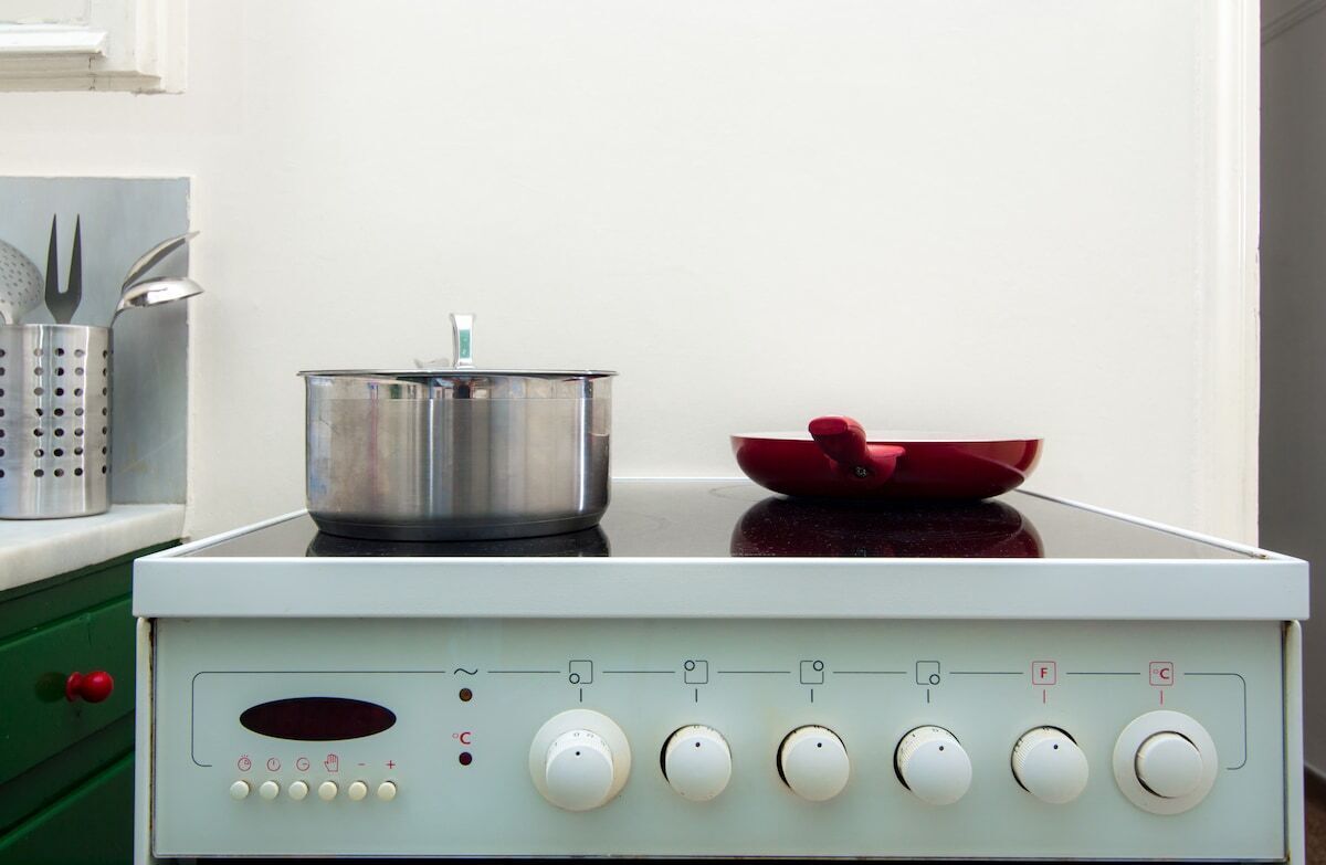 A white electric stove with a pot and a red pan on top.